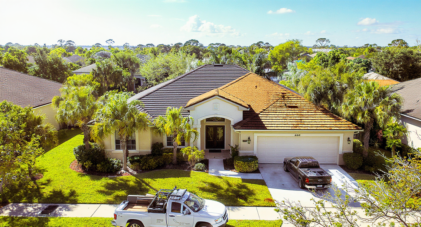 Aerial view of a residential roof replacement in progress on a Southern brick home in South Alabama showing one side stripped to bare plywood decking with peel-and-stick membrane at eaves and the other side freshly shingled with charcoal architectural shingles, illustrating the complete tear-off and installation process used by a licensed roofing contractor in the Gulf Coast 140 to 160 mph wind zone across Mobile County and Baldwin County